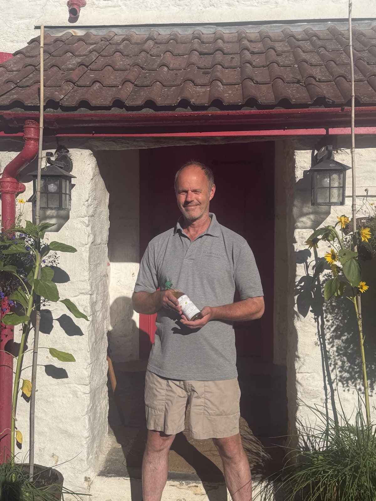 Pete Carling smiling in a whitewashed doorway on a sunny day, holding a bottle of Schniffells