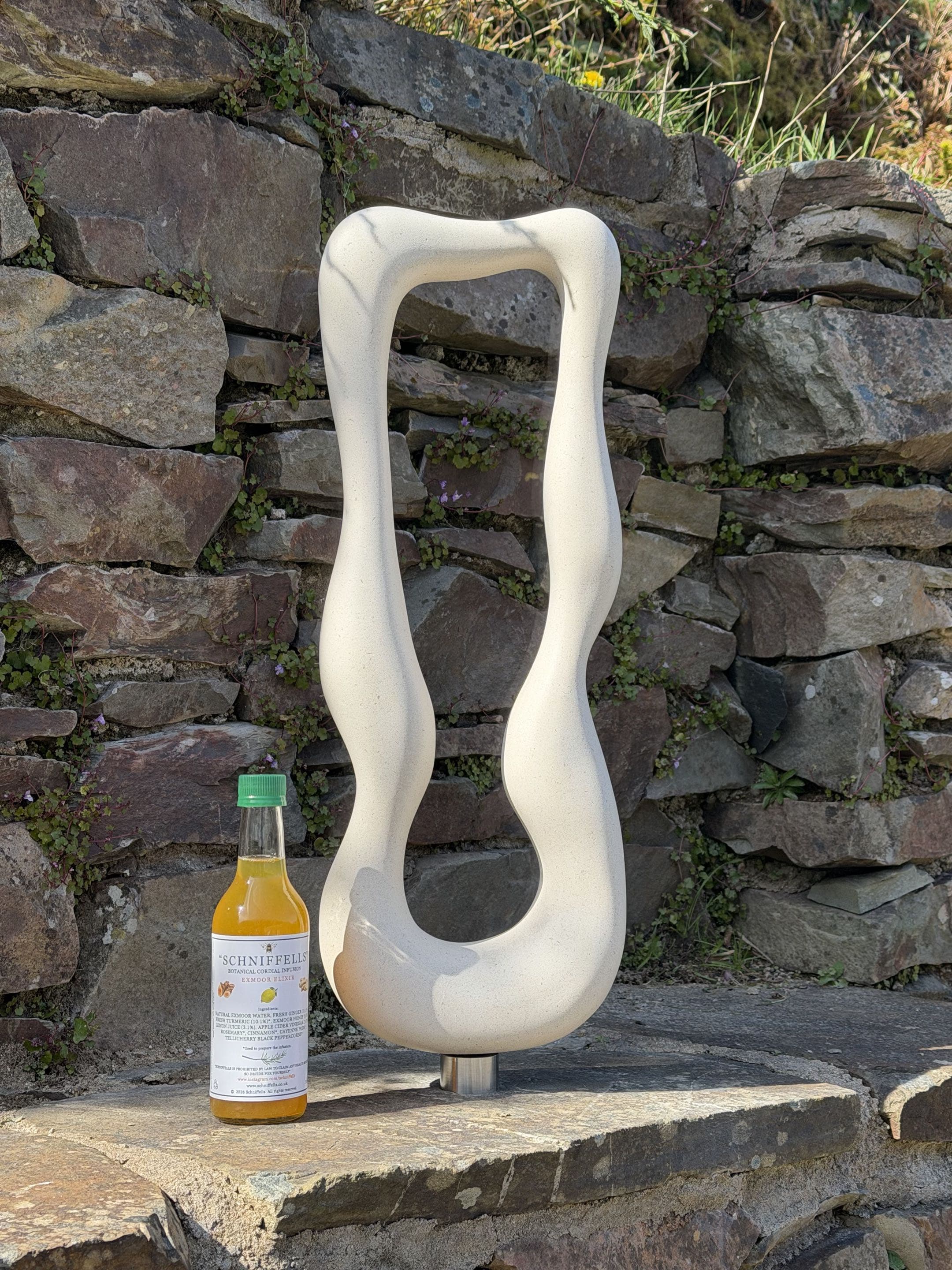 Pete Carling's stone sculpture 'The Kiss 1', a tall carved stone form standing beside a bottle of Schniffells